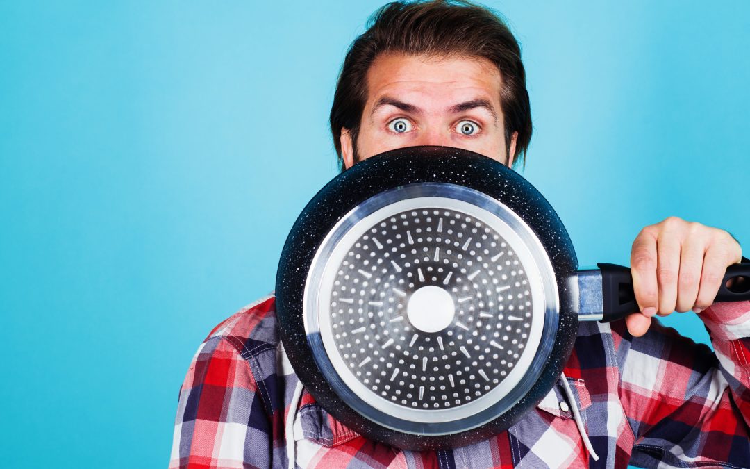 Man holding a frying pan in front of his face, showcasing kitchen tools and supplies relevant to cooking and culinary creativity at Standard Restaurant Supply in Denver.